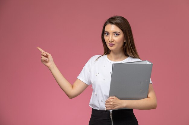 Front view young female in white shirt holding grey colored file on pink wall
