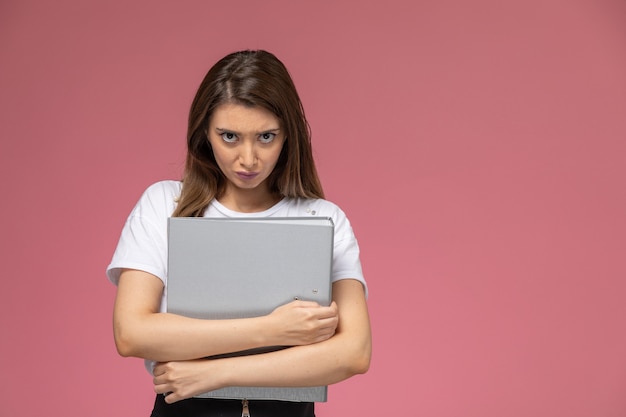 Front view young female in white shirt holding grey document on the pink wall, photo color woman pose model