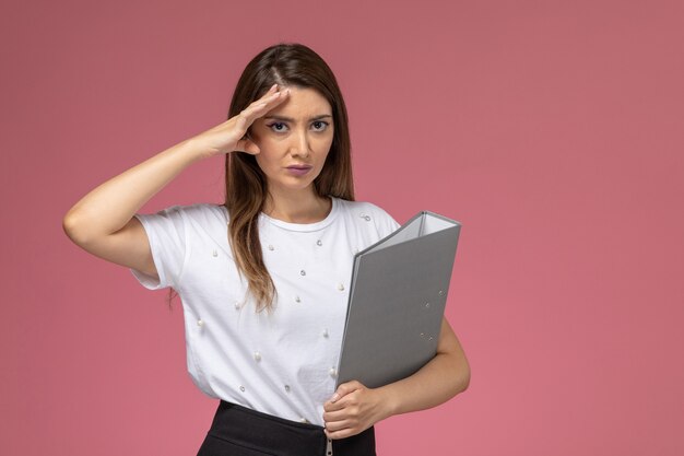 Front view young female in white shirt holding grey file on light pink wall, model woman