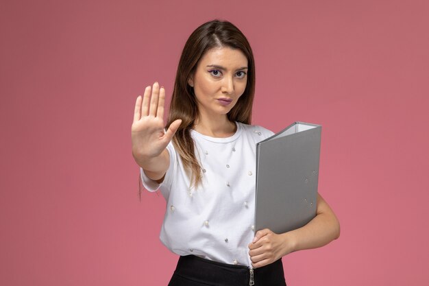 Front view young female in white shirt holding grey file on the pink wall, model woman pose woman