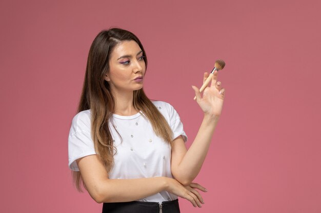 Front view young female in white shirt holding make-up brush on pink wall, color woman pose model woman