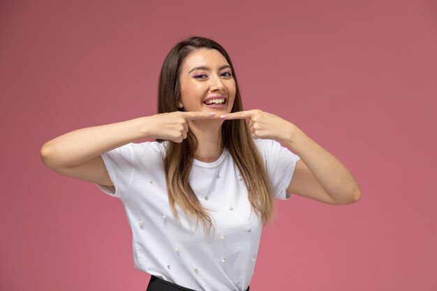 Front view young female in white shirt laughing and touching her acne on the pink wall, color woman pose model