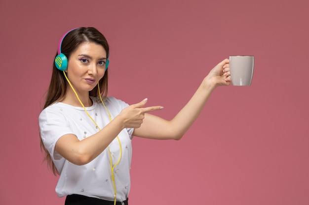 Вид спереди молодая женщина в белой рубашке слушает музыку на розовой стене, цветная модель женщина позы женщина