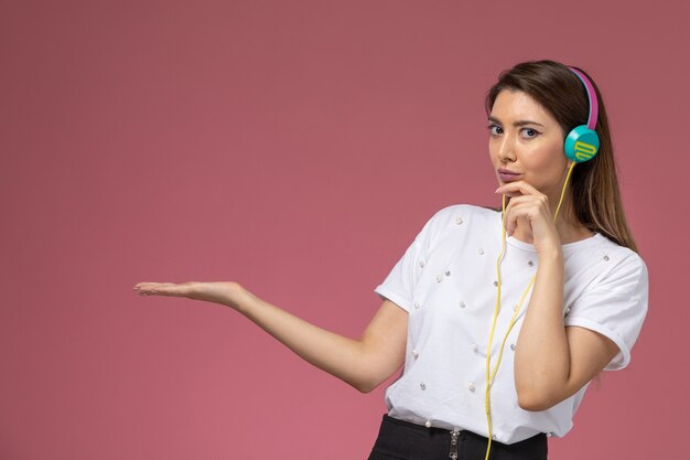 Front view young female in white shirt listening to music on the pink wall, color model woman pose woman