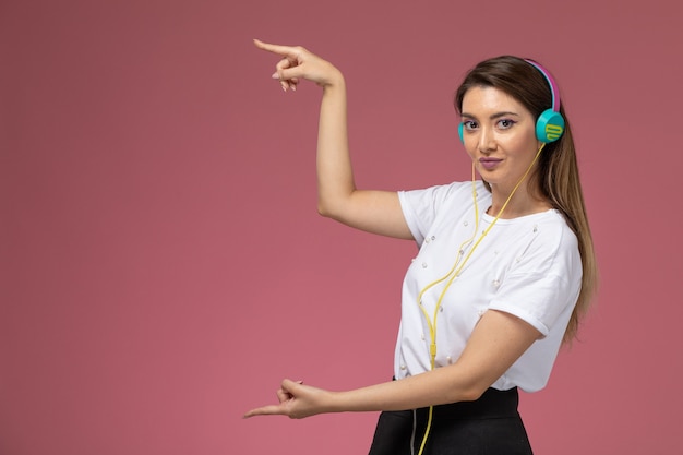 Front view young female in white shirt listening to music on the pink wall, color woman model woman