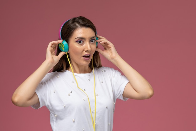 Giovane femmina di vista frontale in camicia bianca che ascolta la musica sulla parete rosa, modello della donna di colore