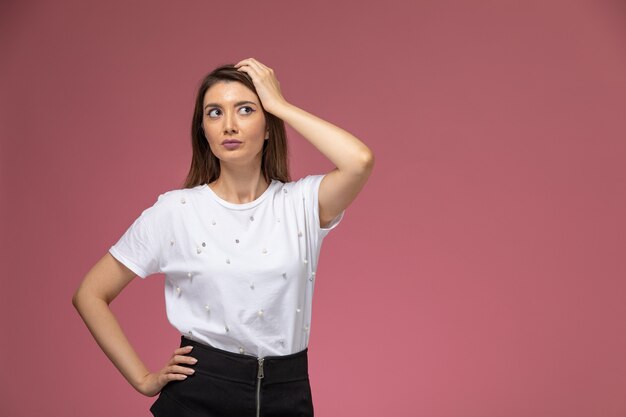 Front view young female in white shirt posing on the pink wall, color woman pose model