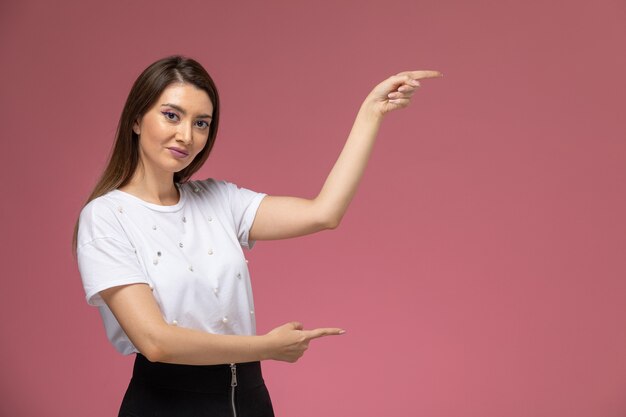 Front view young female in white shirt posing on the pink wall, color woman pose model