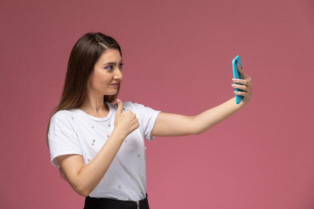 Front view young female in white shirt posing taking selfie on the pink wall, photo color woman pose model