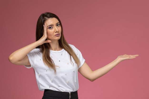 Front view young female in white shirt posing with raised hand on the pink wall, color woman model posing woman