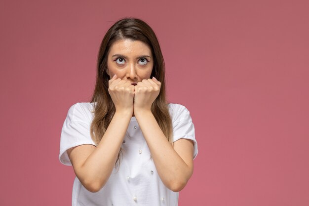 Front view young female in white shirt posing with squeezed fists on the pink wall, color model woman pose