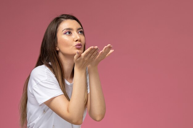 Front view young female in white shirt sending air kisses on the pink wall, color woman model posing woman