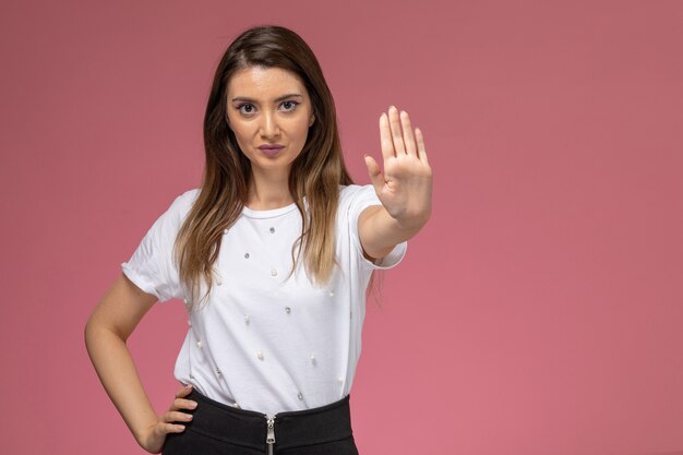 Front view young female in white shirt showing stop sign on pink wall, model woman pose woman