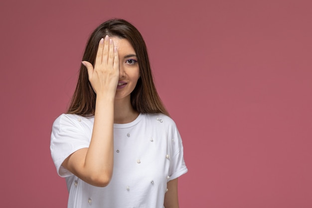 Foto gratuita giovane femmina di vista frontale in camicia bianca che sorride e che copre metà del suo viso sul muro rosa, modello di posa della donna di colore