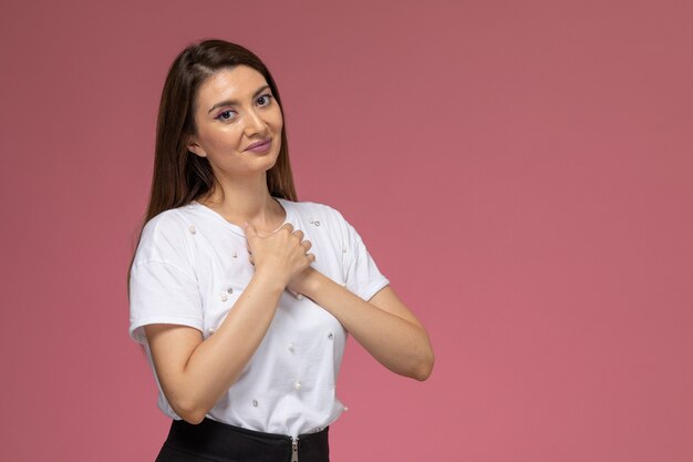 Giovane femmina di vista frontale in camicia bianca che sorride con posa sveglia sulla parete rosa