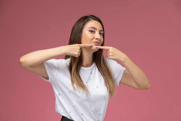 Free photo front view young female in white shirt touching her acne on pink wall, color woman pose model