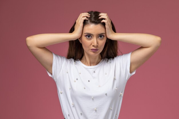 Front view young female in white shirt touching her hair posing on pink wall, model woman