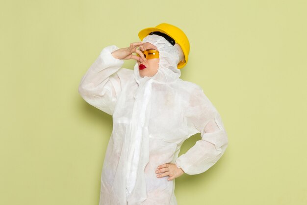 Free photo front view young female in white special suit and yellow helmet holding her nose on the green space