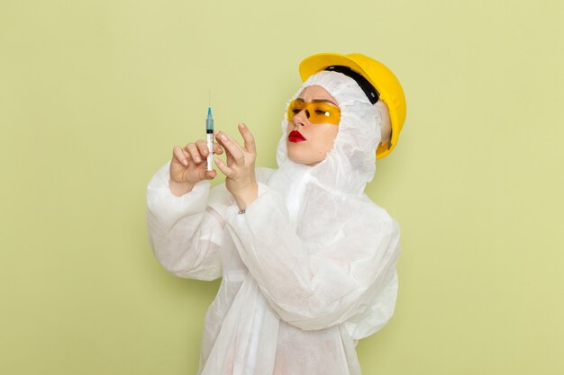 Front view young female in white special suit and yellow helmet holding injection on the green space chemistry work suits