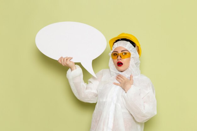 녹색 공간 화학 작업에 큰 흰색 기호를 들고 흰색 특수 양복과 노란색 헬멧에 전면보기 젊은 여성