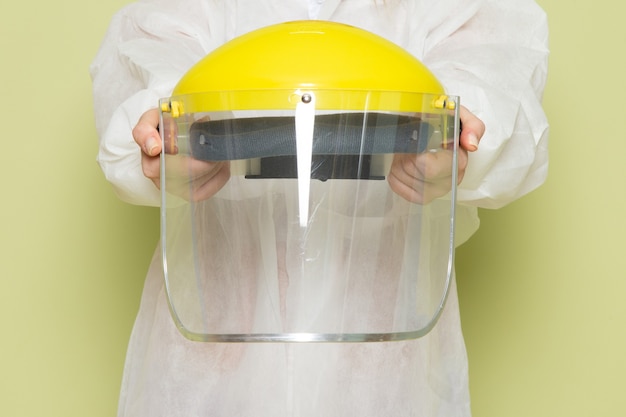 Foto gratuita giovane femmina di vista frontale in vestito speciale bianco e casco giallo che tiene casco protettivo speciale sullo spazio verde