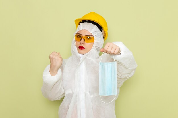 白い特別なスーツと緑の空間化学作業sに滅菌マスクを保持している黄色いヘルメットの正面の若い女性