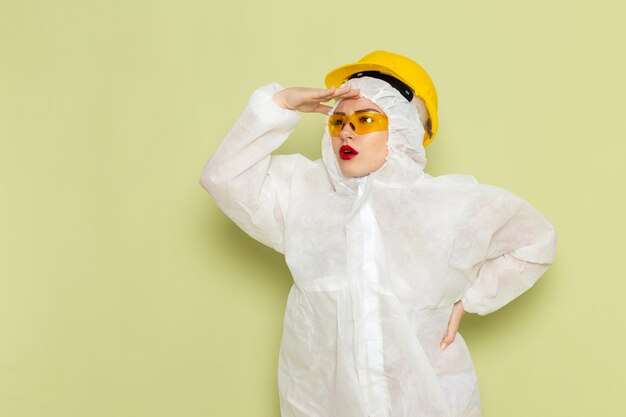 Free photo front view young female in white special suit and yellow helmet looking into the distance on the green space job