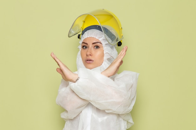흰색 특수 양복과 녹색 공간 작업에 금지 기호를 보여주는 포즈 노란색 헬멧에 전면보기 젊은 여성
