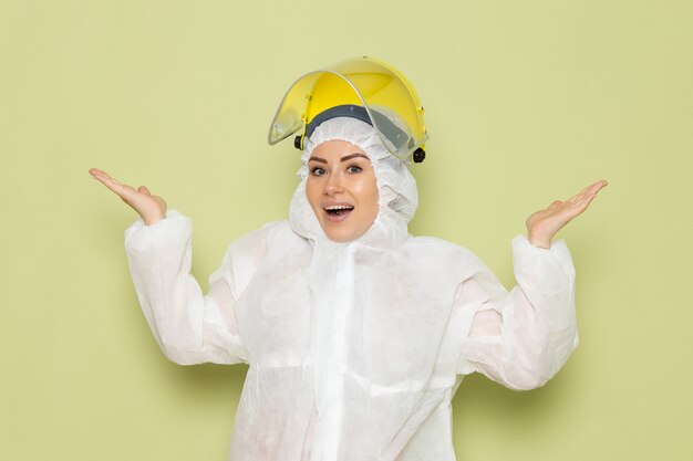 Front view young female in white special suit and yellow helmet posing with delighted expression on the green dsk suit uniform science