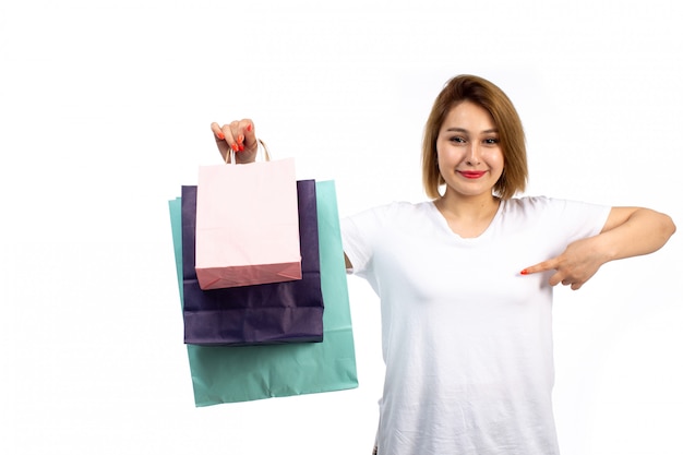 A front view young female in white t-shirt and black jeans holding different colored shopping packages smiling on the white