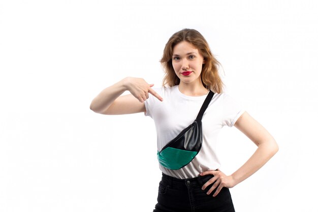 A front view young female in white t-shirt and black jeans wearing little bag on the white