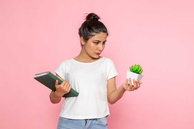 A front view young female in white t-shirt and blue jeans holding copybook and plant