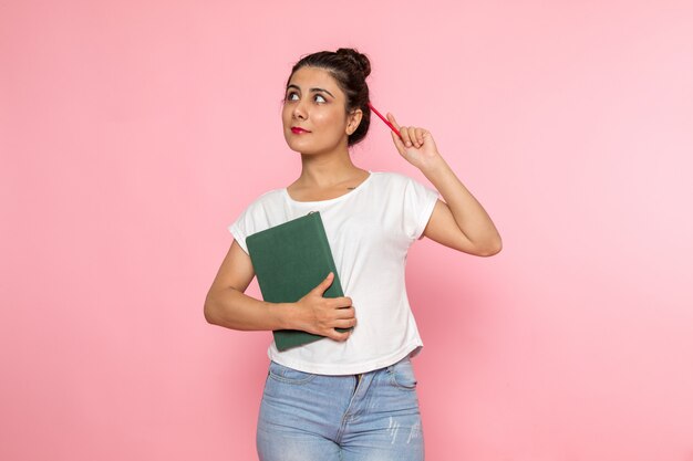A front view young female in white t-shirt and blue jeans holding a copybook with smile