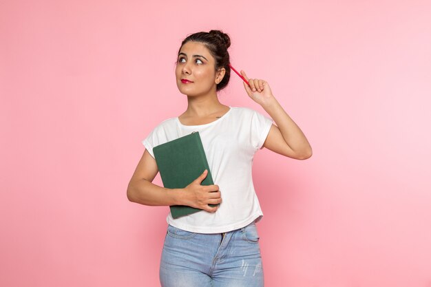 白いtシャツと笑顔でコピーブックを保持しているブルージーンズの正面の若い女性