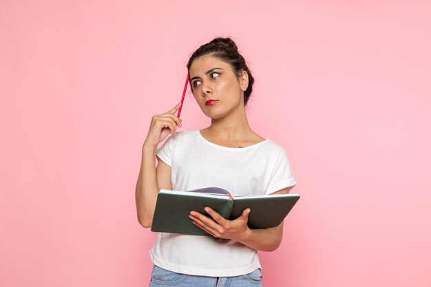 A front view young female in white t-shirt and blue jeans holding copybook with thinking expression