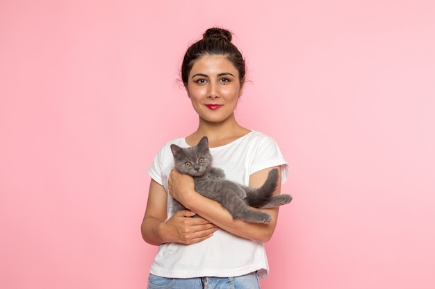 a front view young female in white t-shirt and blue jeans holding cute grey kitten with smile