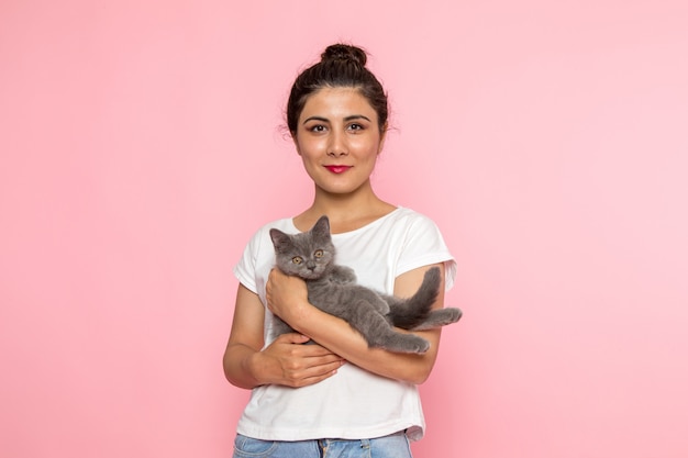 Foto gratuita una giovane femmina di vista frontale in maglietta bianca e blue jeans che tengono gattino grigio sveglio con il sorriso