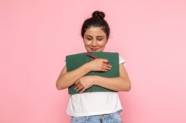 A front view young female in white t-shirt and blue jeans holding green copybook with smile