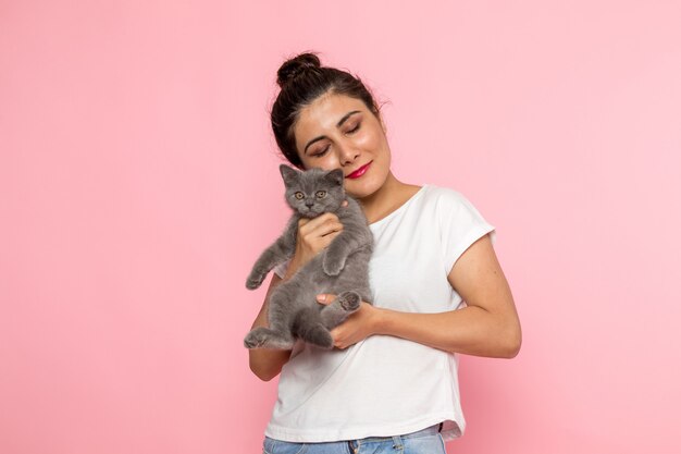 a front view young female in white t-shirt and blue jeans holding little cute grey kitten