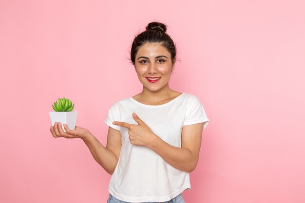 白いtシャツと小さな植物を保持しているブルージーンズの正面の若い女性