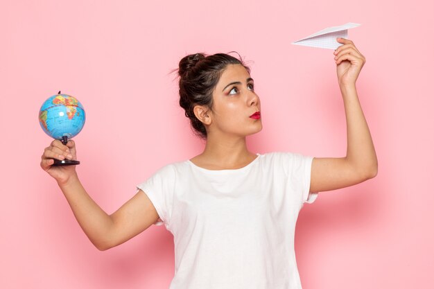 A front view young female in white t-shirt and blue jeans holding paper plane and little globe