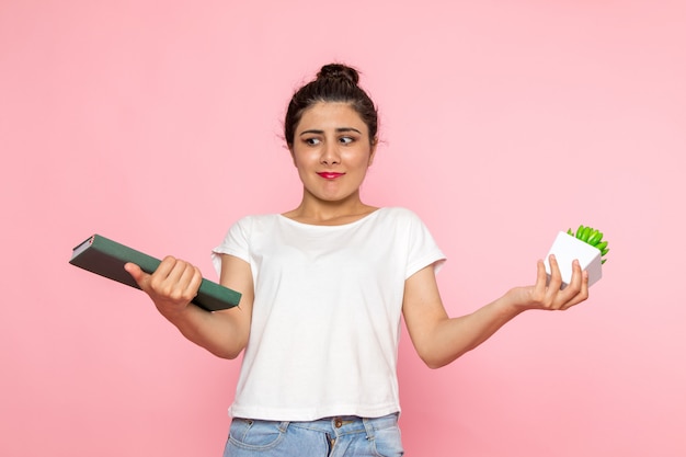 A front view young female in white t-shirt and blue jeans holding plant and copybook