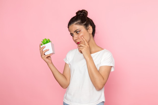 白いtシャツとブルージーンズの植物を保持している正面の若い女性