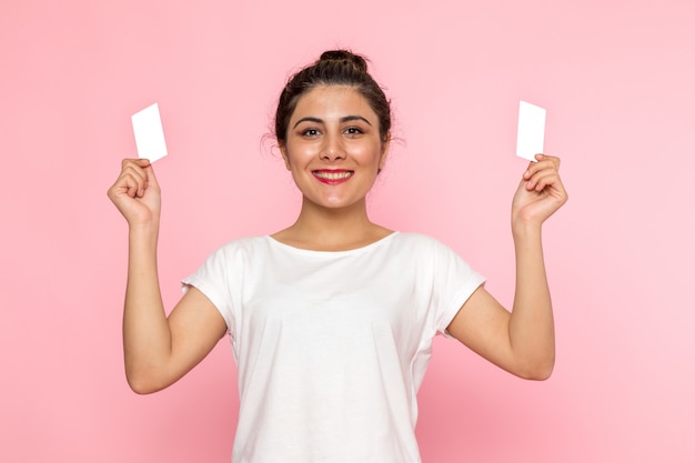 A front view young female in white t-shirt and blue jeans holding white cards