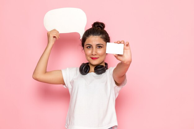 A front view young female in white t-shirt and blue jeans holding white sign and card