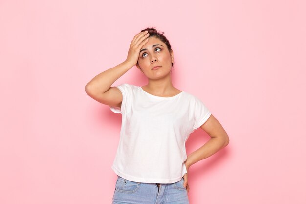 A front view young female in white t-shirt and blue jeans posing holding her forehead