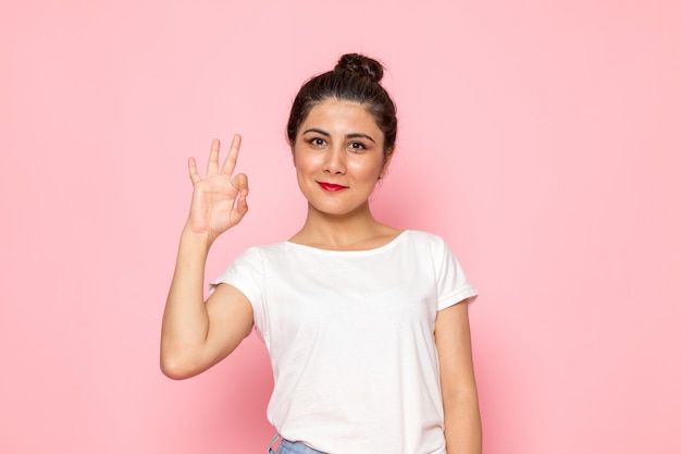 Una giovane femmina di vista frontale in maglietta e blue jeans bianche che posano con l'espressione contentissima