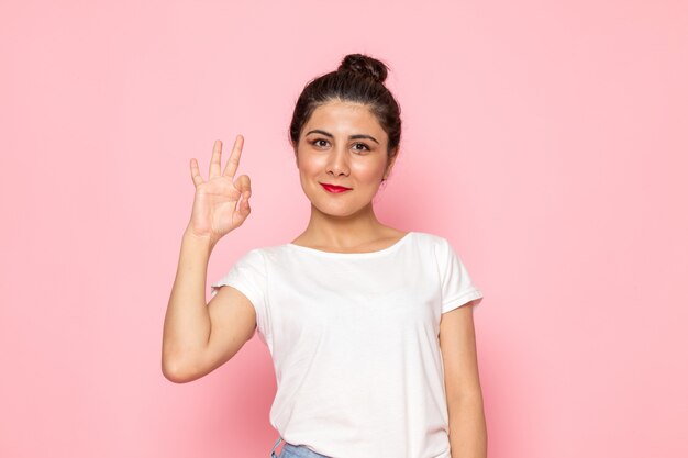 A front view young female in white t-shirt and blue jeans posing with delighted expression