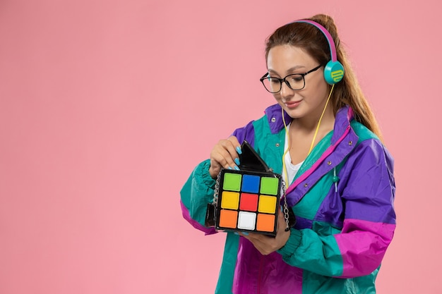 ピンクの背景のヘッドフォンを介して音楽を聴く白いtシャツ色のコートで正面の若い女性