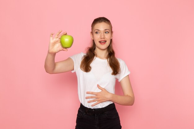 밝은 분홍색 벽에 신선한 녹색 사과를 들고 흰색 티셔츠에 젊은 여성의 전면보기
